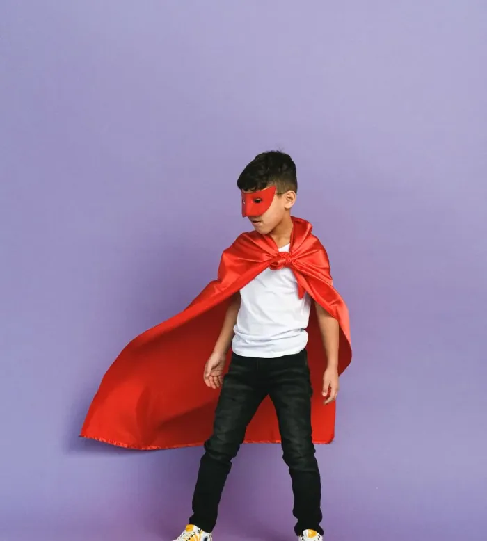 A child in a red cape and mask standing like a superhero