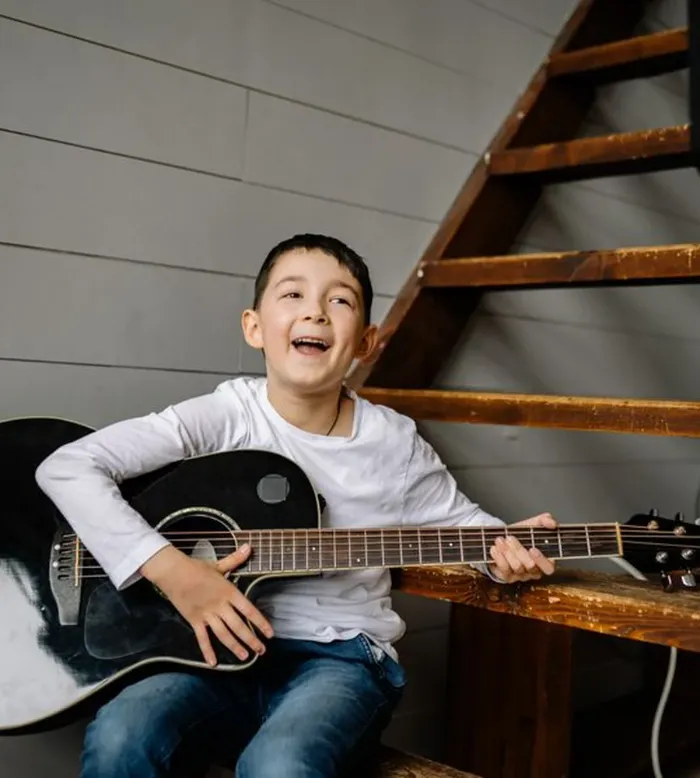 A cheerful boy playing an acoustic guitar at home