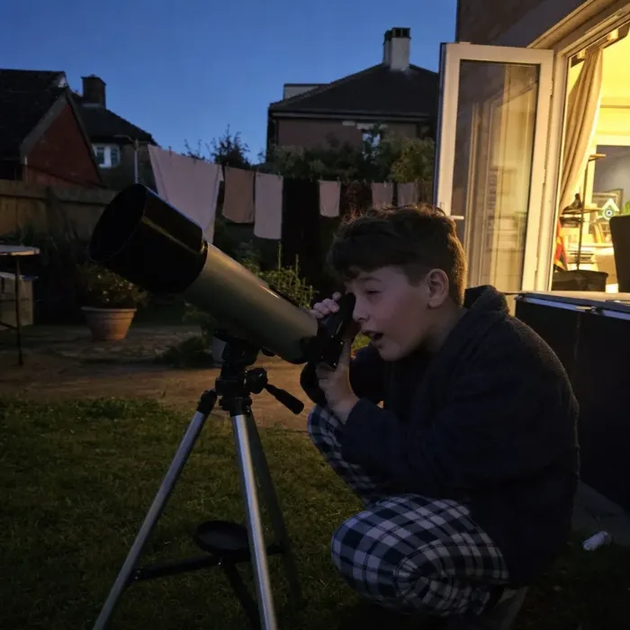 A boy looking through a telescope at dusk in the backyard